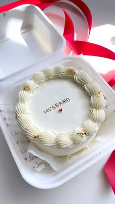 a white cake sitting on top of a plastic container next to a red and white ribbon