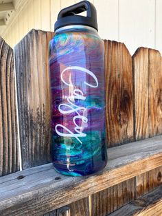 a purple and blue water bottle sitting on top of a wooden bench next to a fence