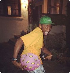 a man in a yellow shirt and green hat with his mouth open, standing outside at night