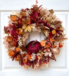 a wreath with leaves, berries and an apple is hanging on the front door handle