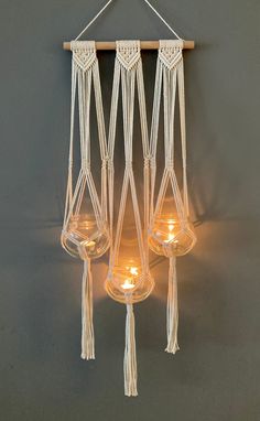 three hanging candles with rope and glass holders on the wall, one is lit up