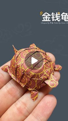 a hand holding an origami turtle in it's left hand, with chinese characters on the background