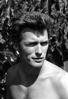 black and white photograph of a shirtless man in front of a bush with his eyes closed