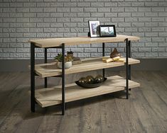 a table with shelves and pictures on it in front of a brick wall, next to a potted plant