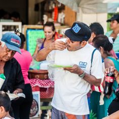 a man eating food from a plate while standing next to other people at an outdoor market