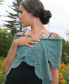 a woman wearing a green knitted shawl in front of some wildflowers