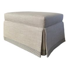 an upholstered ottoman with pleated trim on the top and bottom, in grey linen