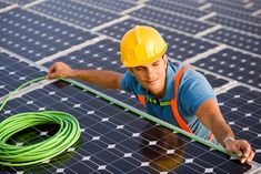 a man in hard hat and safety vest working on solar panel with green hose next to it