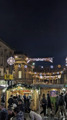 many people are walking around in the city at christmas time with lights and decorations all around