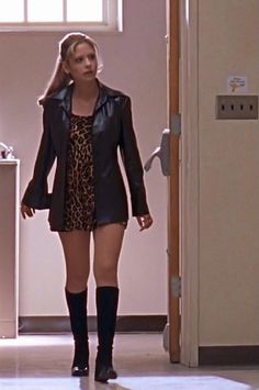 a woman in a short dress and black jacket walking into a room with an open door