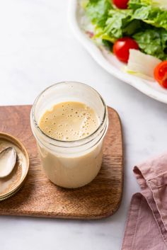 a glass jar filled with dressing next to a salad on a cutting board and spoon