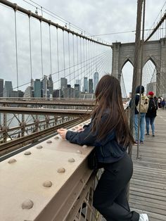 a woman standing on the side of a bridge looking at her cell phone while others walk by