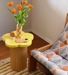 a yellow table with orange flowers on it and a chair in the corner next to it