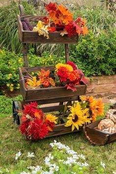 three tiered wooden trays filled with flowers and vegetables on the grass in front of a garden