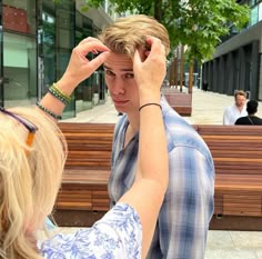 a young man adjusts his hair while standing next to a woman on a bench