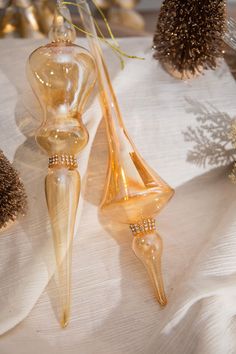 two glass vases sitting next to each other on a white cloth covered tablecloth