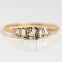 a gold ring with green and white stones on the side, sitting on a white surface