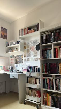 a book shelf filled with lots of books next to a white desk and computer monitor