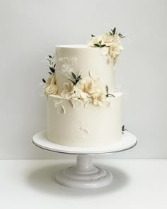 a three tiered cake with white frosting and flowers on the top is sitting on a pedestal