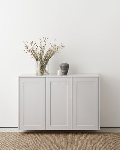 two vases sitting on top of a white cabinet next to a rug and wall