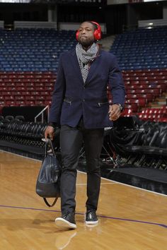 a man wearing headphones walking on a basketball court with a handbag in his mouth