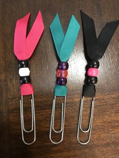 three different colored lanyards with metal clips on a wooden table and one is black, the other has pink, blue, and green