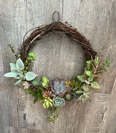 a wreath with succulents and greenery hanging on a wooden wall