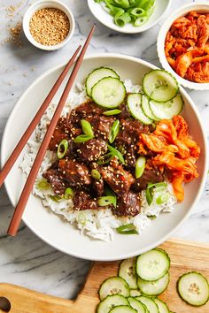 a white plate topped with meat and veggies next to chopsticks on top of rice