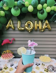 a person holding a cup in front of a table filled with desserts and balloons