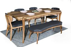 a wooden table with blue chairs and plates on it, sitting on a rug in front of a white wall