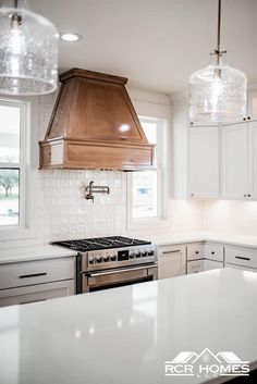 a kitchen with white cabinets and stainless steel stove top oven in the center, two pendant lights hanging from the ceiling