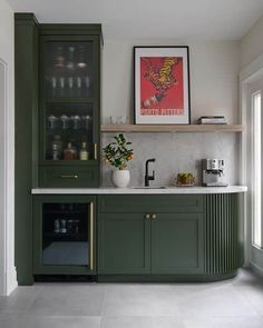 a kitchen with green cabinets and marble counter tops, an art print on the wall