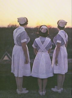 three women in white dresses and hats looking at the sunset