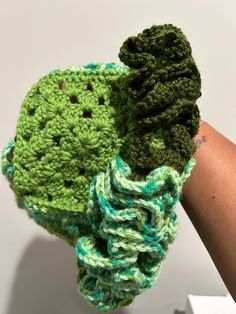 a green crocheted object is held up by someone's arm