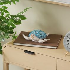 an alarm clock sitting on top of a wooden table next to a book and potted plant