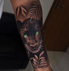 a black cat with green eyes and leaves on his leg is seen in this tattoo design