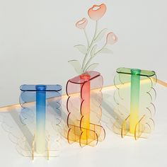 three colorful vases with flowers in them sitting on a table next to each other