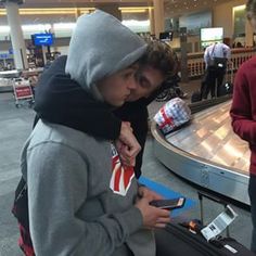 two people standing in an airport looking at their cell phones