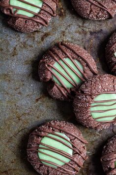 chocolate cookies with green frosting and drizzled in the middle on a baking sheet