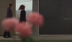 two people standing in front of a door with pink flowers on the ground next to them