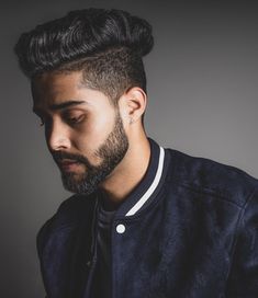 a man with a beard wearing a jacket and looking at his cell phone while standing in front of a gray background