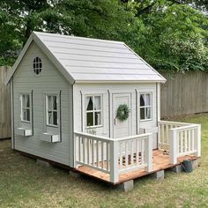 a small gray house sitting on top of a wooden platform in the grass next to a fence