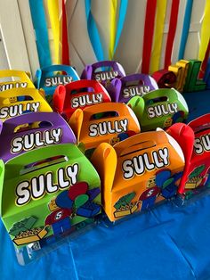 colorful candy boxes are lined up on a blue tablecloth with balloons in the background