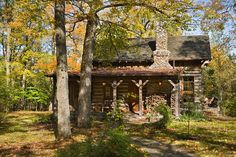 an old log cabin in the woods surrounded by trees and leaves with fall foliage around it