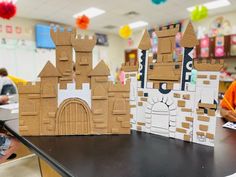 two cardboard castles sitting on top of a table in front of some children's artwork