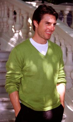 a man in a green sweater standing next to a white stair case and looking at the camera