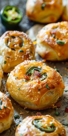 several different types of breads on a baking sheet with pepperoni and jalapenos in the background