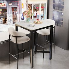 two white chairs sitting at a table in front of a store window with flowers on it