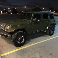 a green jeep is parked in a parking lot at night with its lights turned on