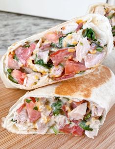 two burritos with meat, cheese and veggies sitting on a cutting board